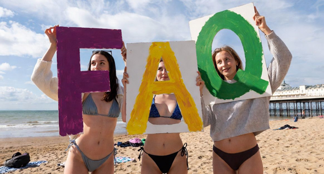 Tres participantes en la playa de Bournemouth sostienen carteles FAQ durante un viaje de idiomas con LISA! en Inglaterra