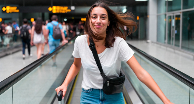 Viajes de idiomas con LISA! – viaje, aeropuerto y comienzo de la aventura Joven con maleta en el aeropuerto durante un viaje de idiomas con LISA! emocionada por la llegada
