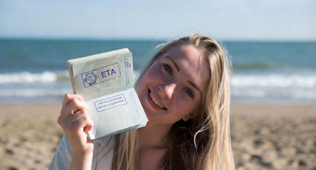 Viajes de idiomas en Inglaterra con LISA! – entrada, visado ETA y preparación Mujer en la playa mostrando pasaporte con autorización ETA durante un viaje de idiomas con LISA! a Inglaterra
