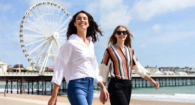 Viajes de idiomas para adultos en Inglaterra Bournemouth con LISA! – paseo marítimo, mar y atracciones Dos participantes caminando por el paseo marítimo en Bournemouth con la noria durante un viaje de idiomas con LISA! en Inglaterra