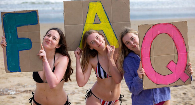 Preguntas frecuentes sobre viajes de idiomas en Inglaterra Bournemouth con LISA! – preguntas y respuestas Tres participantes en la playa de Bournemouth sostienen carteles FAQ durante un viaje de idiomas con LISA! en Inglaterra