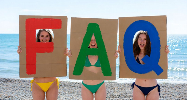  Tres participantes en la playa de Brighton sostienen carteles FAQ durante un viaje de idiomas con LISA! en Inglaterra