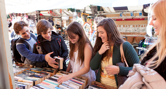 Viajes de idiomas en Inglaterra Cambridge City con LISA! – ocio, compras y experiencias locales Adultos comprando en un mercado en Cambridge City Inglaterra durante un viaje de idiomas con LISA! explorando libros y disfrutando del tiempo libre