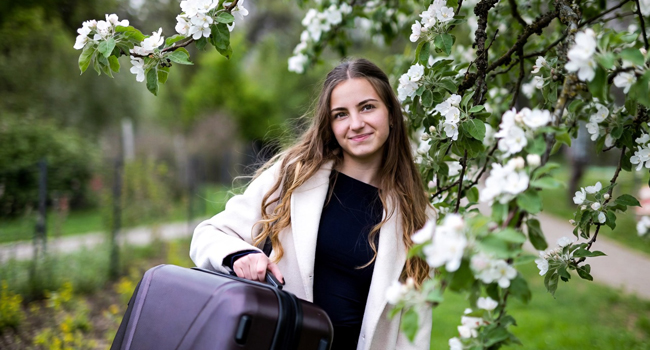 Reserva de un viaje de idiomas con LISA! – una chica con una maleta. Una chica con una maleta bajo un manzano local simboliza la reserva de un viaje de idiomas con LISA!