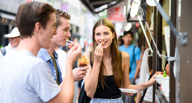 Vacaciones educativas Osaka Japón con LISA! – aprender japonés, street food y experiencias auténticas Adultos probando comida callejera en Osaka durante unas vacaciones educativas con LISA! descubriendo la gastronomía japonesa y la vida urbana internacional