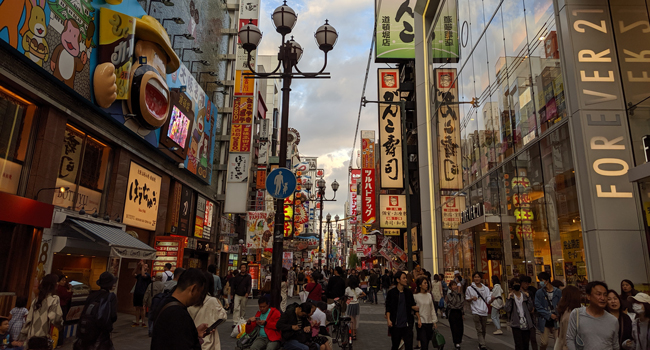 Vacaciones educativas Osaka Japón con LISA! – aprender japonés, ciudad y experiencias auténticas Calle animada en Osaka durante unas vacaciones educativas con LISA! mostrando cultura japonesa, luces de neón y vida urbana