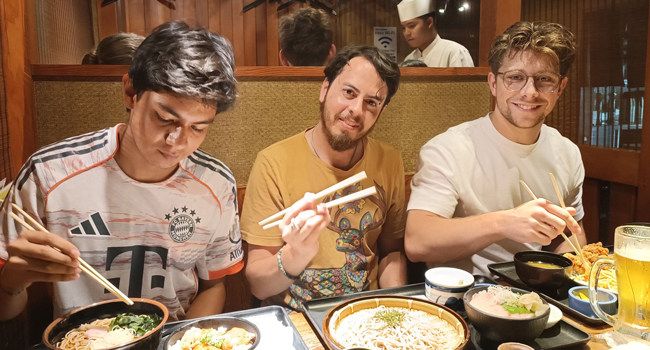 Adultos disfrutando de comida japonesa en Tokio durante un viaje de idiomas con LISA! experimentando la cultura con palillos