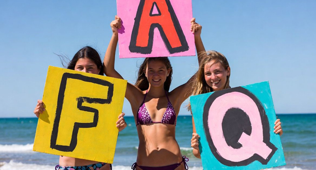 Tres estudiantes en la playa en Bournemouth sostienen carteles FAQ durante un viaje de idiomas con LISA!