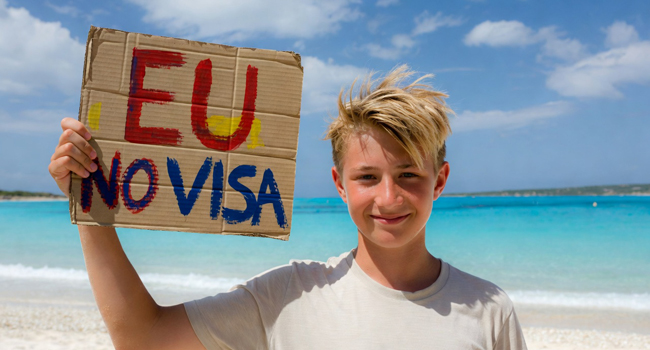 Viajes de idiomas de inglés en Malta para estudiantes sin visado para ciudadanos de la UE Estudiantes de un viaje de idiomas de inglés en Malta en la playa con un cartel sobre la entrada sin visado para ciudadanos de la UE