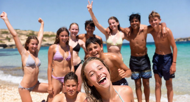 Diez adolescentes en la playa en Malta San Gwann durante el programa de actividades con los brazos levantados