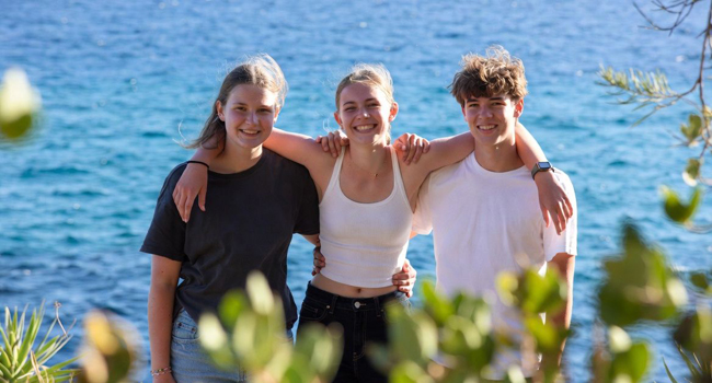 Tres estudiantes junto al mar abrazándose en amistad durante un viaje de idiomas en Malta San Gwann