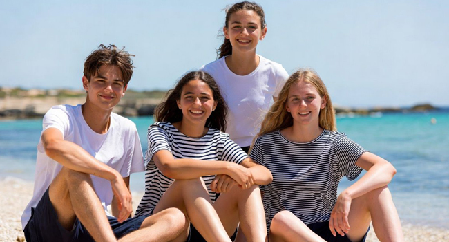 Viajes de idiomas para estudiantes en Malta con LISA! – grupo de estudiantes en la playa Cuatro estudiantes sentados en la playa en Malta durante un viaje de idiomas con LISA! para estudiantes