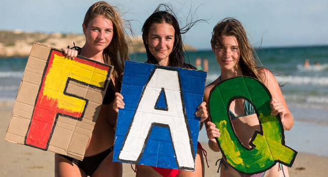 Preguntas frecuentes sobre viajes de idiomas para estudiantes en Malta con LISA! – estudiantes con letras junto al mar Tres estudiantes en la playa en Malta sostienen grandes letras FAQ durante un viaje de idiomas con LISA! para estudiantes