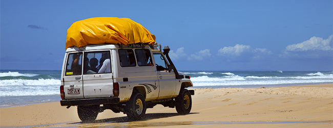 Geländewagen am Strand von Australien während einer LISA! Sprachreise Geländewagen fährt entlang des Strandes mit Wellengang im Hintergrund in Australien während einer Sprachreise