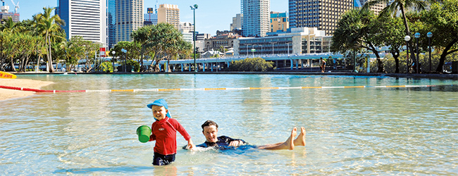 Familienfreundlicher Strand in Brisbane während einer LISA! Sprachreise Kinder spielen im flachen Wasser mit Stadtblick im Hintergrund in Brisbane während einer LISA! Sprachreise