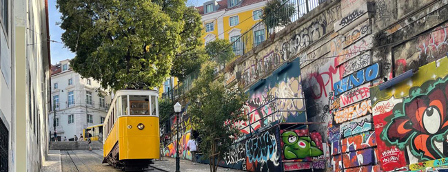 Strasse in Lissabon mit gelber Strassenbahn, die einen Hügel hinauffährt