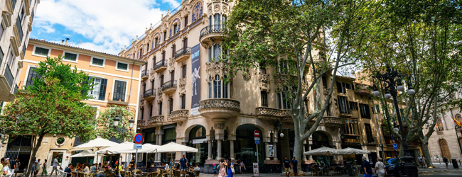 Menschen sitzen und laufen über einen Platz in der Altstadt von Palma de Mallorca mit Cafes und Geschäften