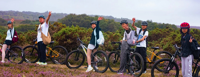 Ausflug mit Fahrrädern in englischer Landschaft bei Adventure England Schüler auf Fahrrädern winken in die Kamera vor einer englischen Landschaft