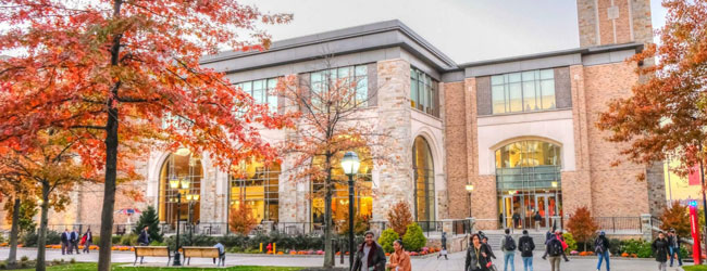 Gebäude der St. John's University in New York - Ort für Schülersprachreisen Ein Backsteingebäude mit Bäumen im Herbstlaub und Menschen davor